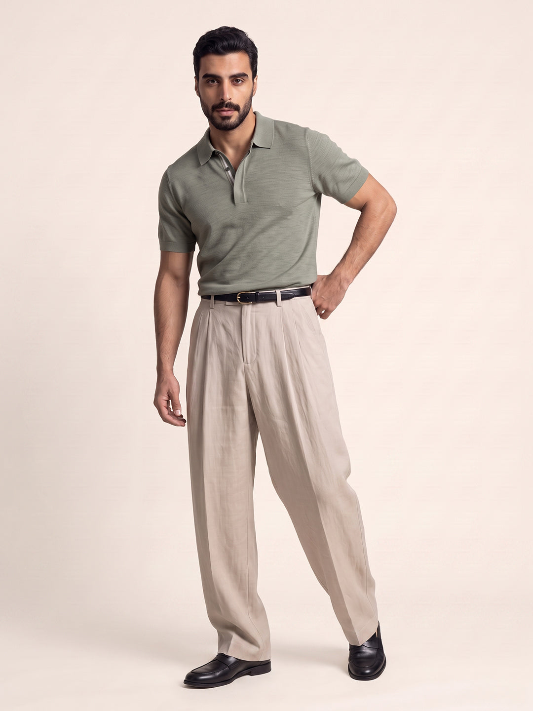 #soft-sage_group A man modeling a short-sleeve olive green polo shirt paired with light beige trousers, a black belt, and black dress shoes, standing against a solid light beige studio background.