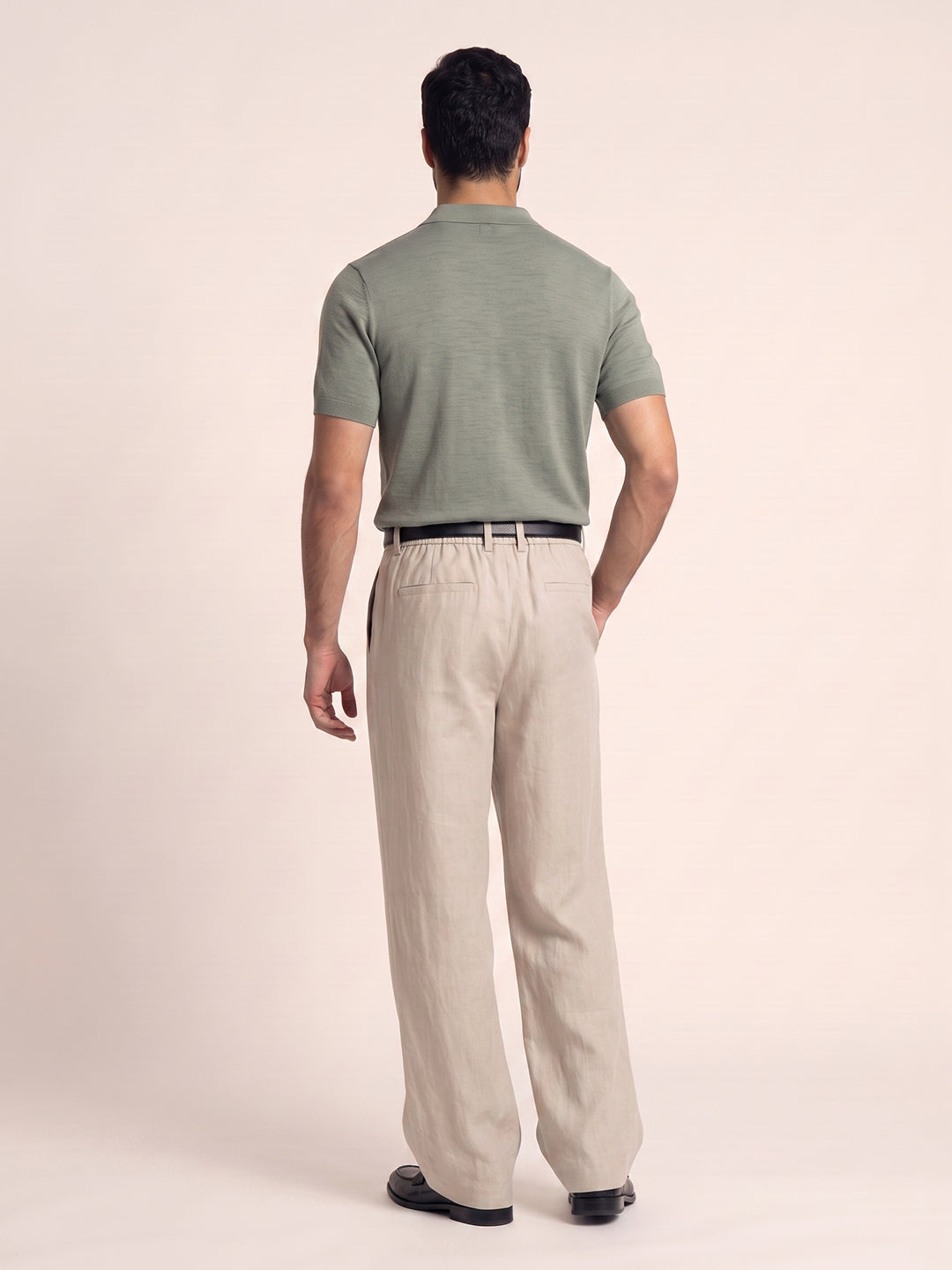 #soft-sage_group A man viewed from behind wearing a muted sage green short-sleeve polo shirt and light beige trousers, standing against a solid pale peach studio background.