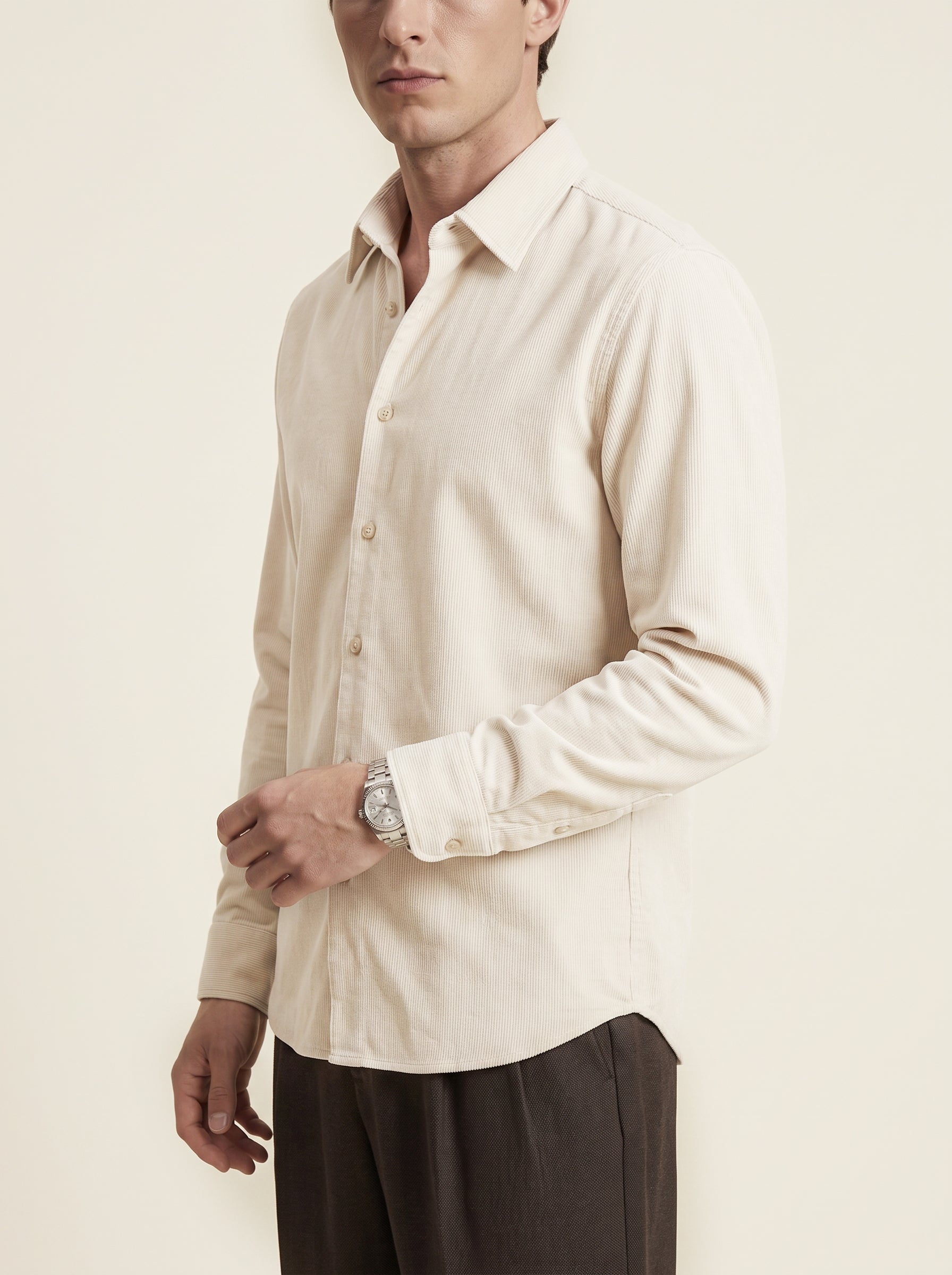 #Ecru-Ivory_group  A man wearing a light beige long-sleeve linen button-down shirt and dark brown trousers, shown from the chest down against a solid cream background.
