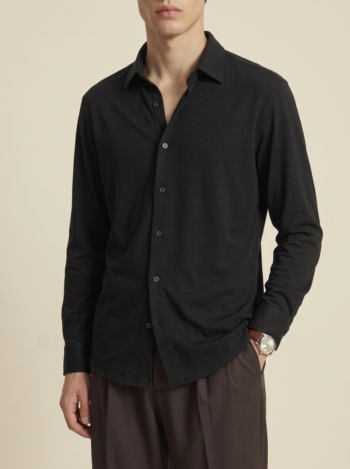 #Jet-Black_group A man wearing a black long-sleeve button-up shirt and dark brown trousers, shown from a side-back angle against a plain beige studio background.