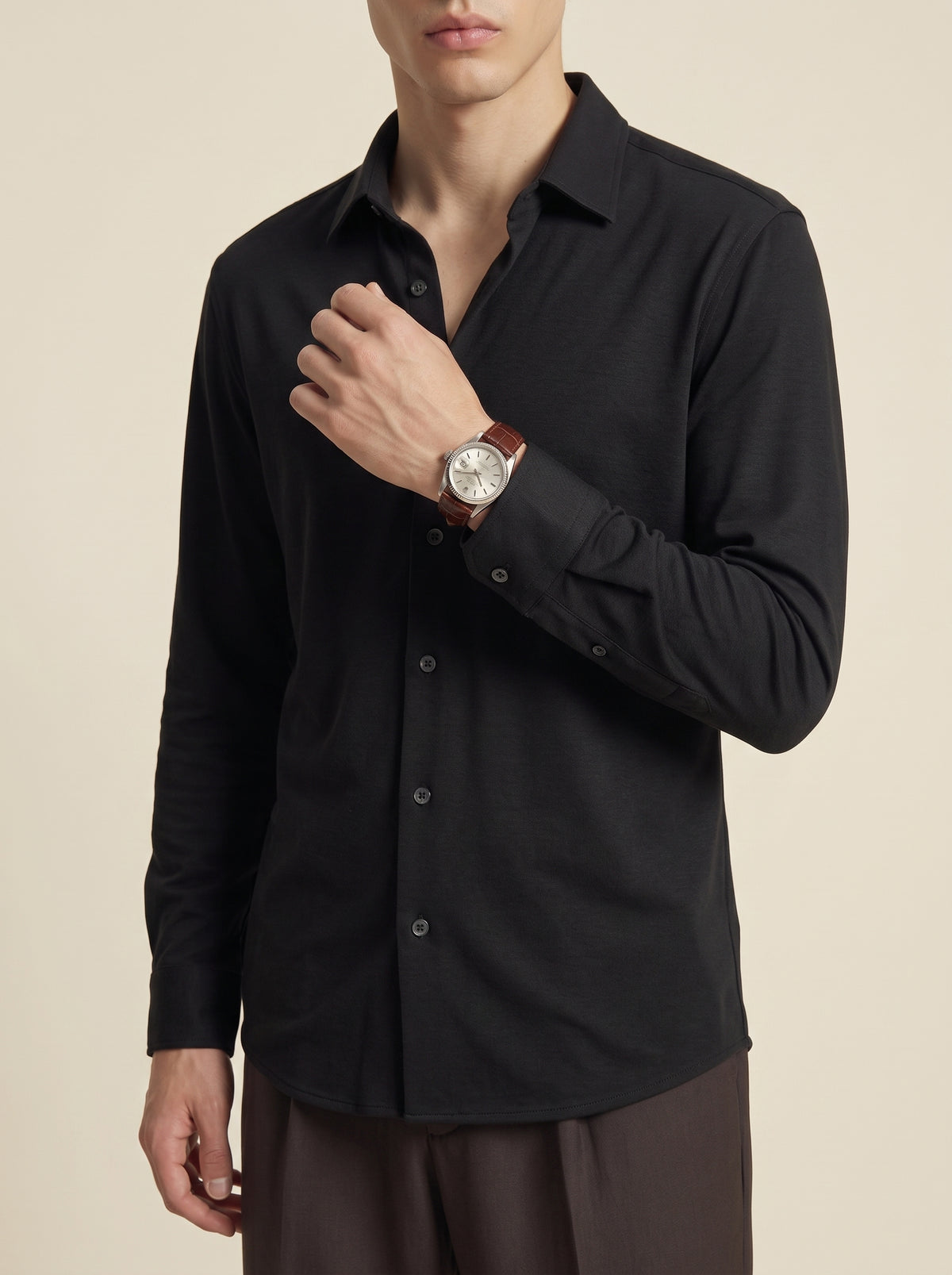 #Jet-Black_group A man wearing a black long-sleeve button-up shirt and dark brown trousers, shown from a side-back angle against a plain beige studio background.