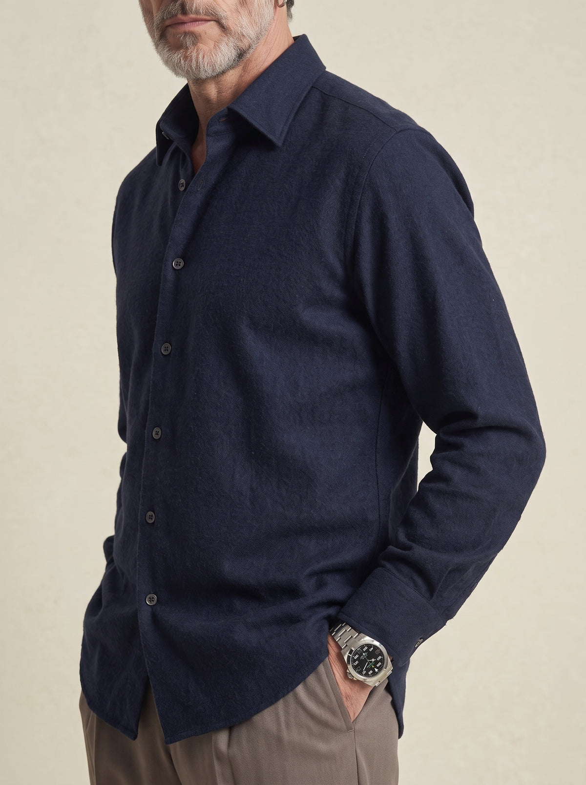#Blue-Navy_group A man wearing a dark navy blue long-sleeve linen button-down shirt, paired with khaki trousers and a silver watch, shown from the waist up against a neutral beige background.