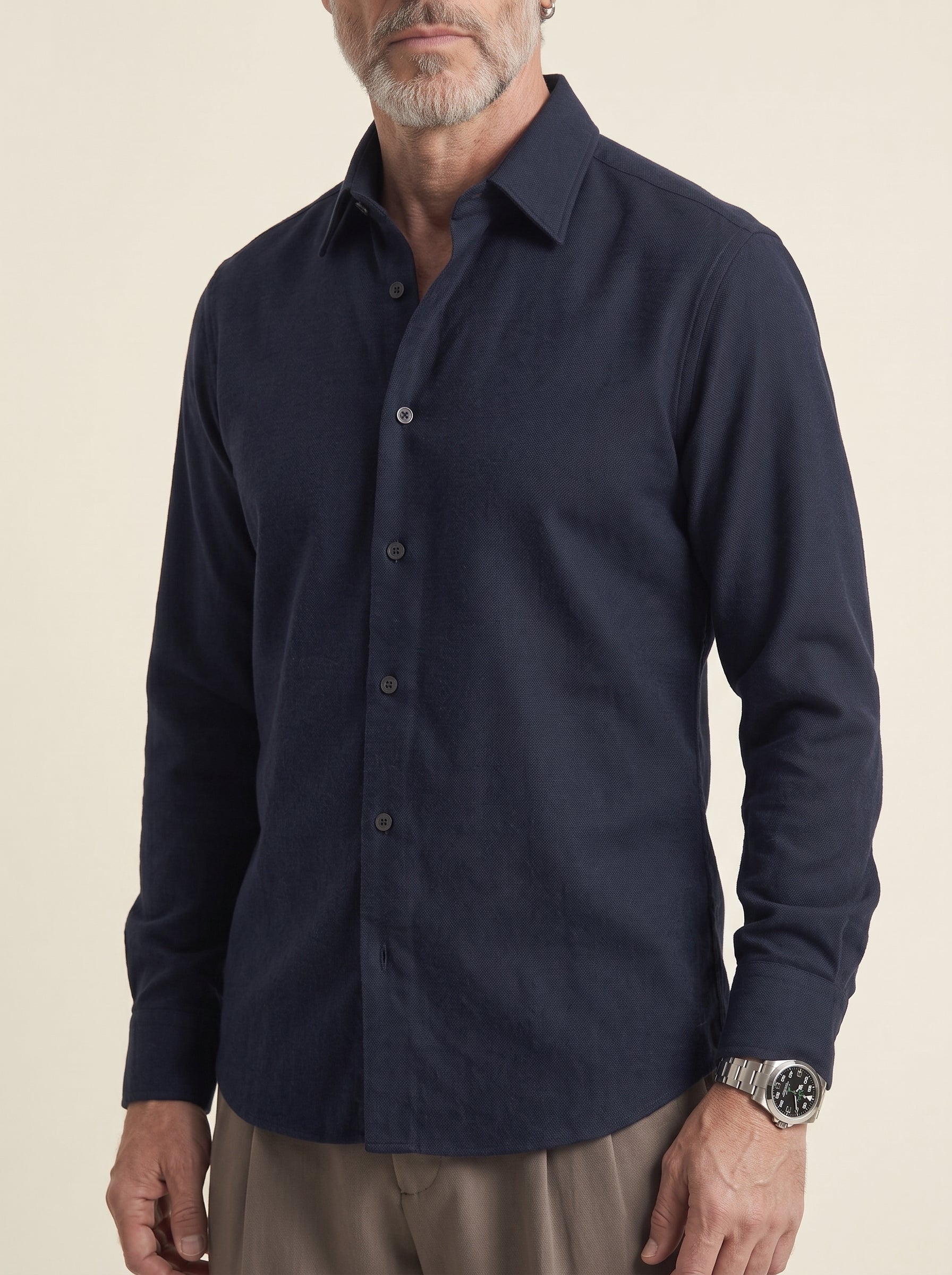 #Blue-Navy_group A man wearing a dark navy blue long-sleeve button-down shirt, paired with khaki pants, shown from the chin down against a plain beige background.