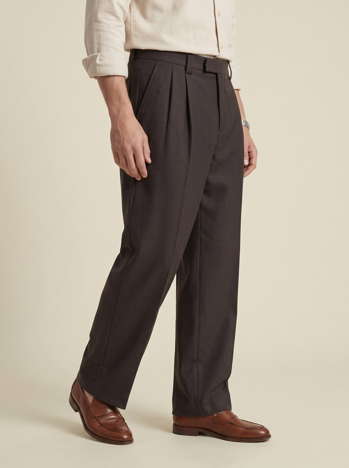 #Cedar-Brown_group A person wearing dark charcoal pleated trousers with a cream shirt and brown leather dress shoes, shown from the waist down against a plain beige studio background.