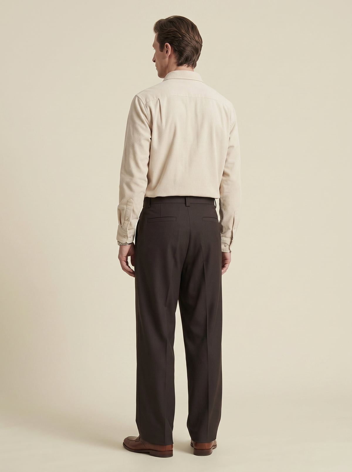 #Cedar-Brown_group A man viewed from the back wearing a light cream long-sleeve button-down shirt and dark charcoal gray trousers, standing against a solid light beige background.