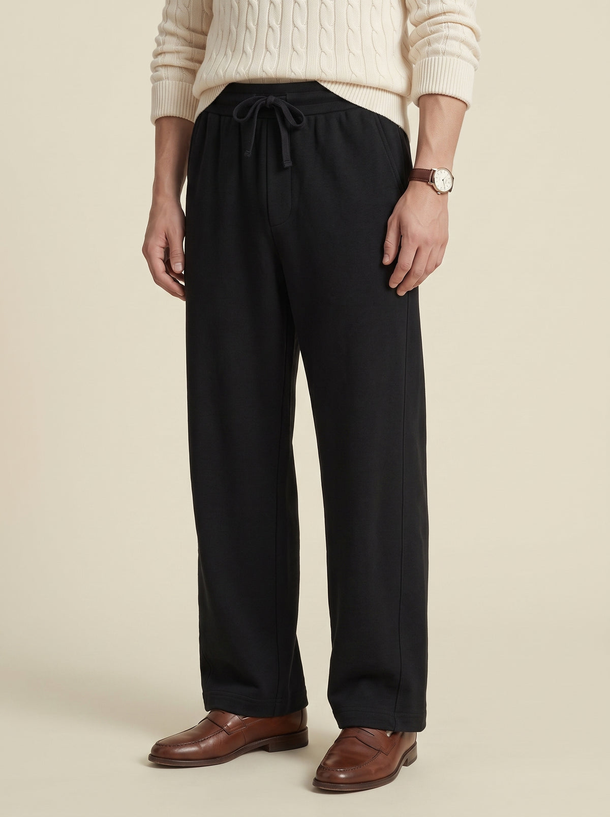 #Jet-Black_group A person wearing black wide-leg drawstring trousers, a cream cable-knit sweater, and brown leather shoes, standing against a plain beige studio background.