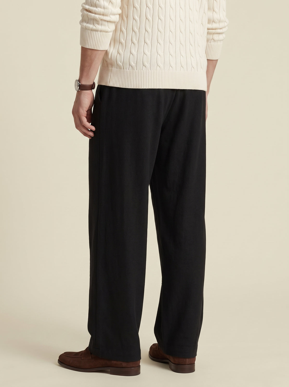 #Jet-Black_group A person shown from the back wearing black wide-leg trousers, a cream cable-knit sweater, and brown shoes against a plain beige studio background.