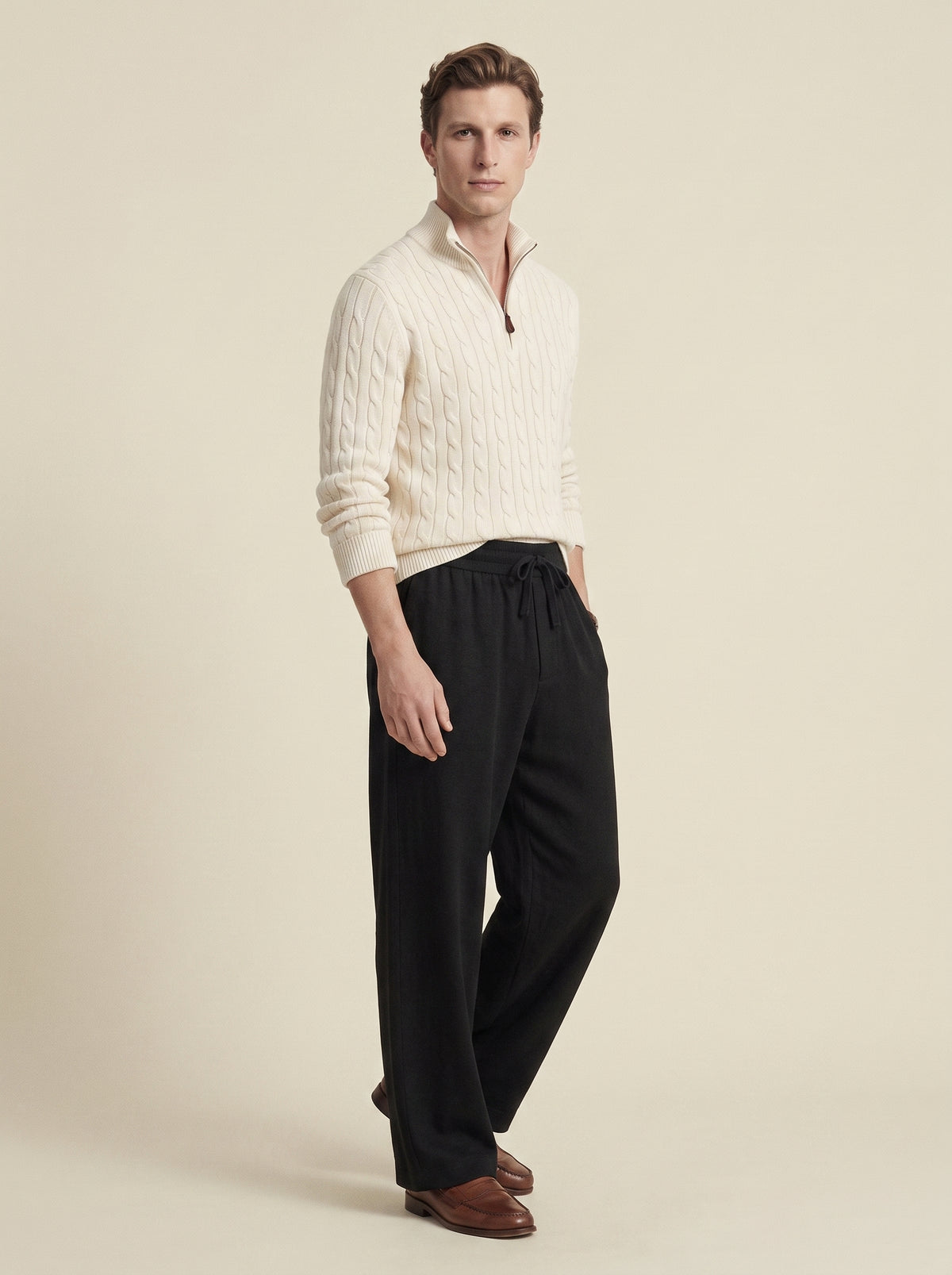 #Jet-Black_group A man modeling a cream cable-knit quarter-zip sweater and black drawstring trousers against a solid beige studio background.
