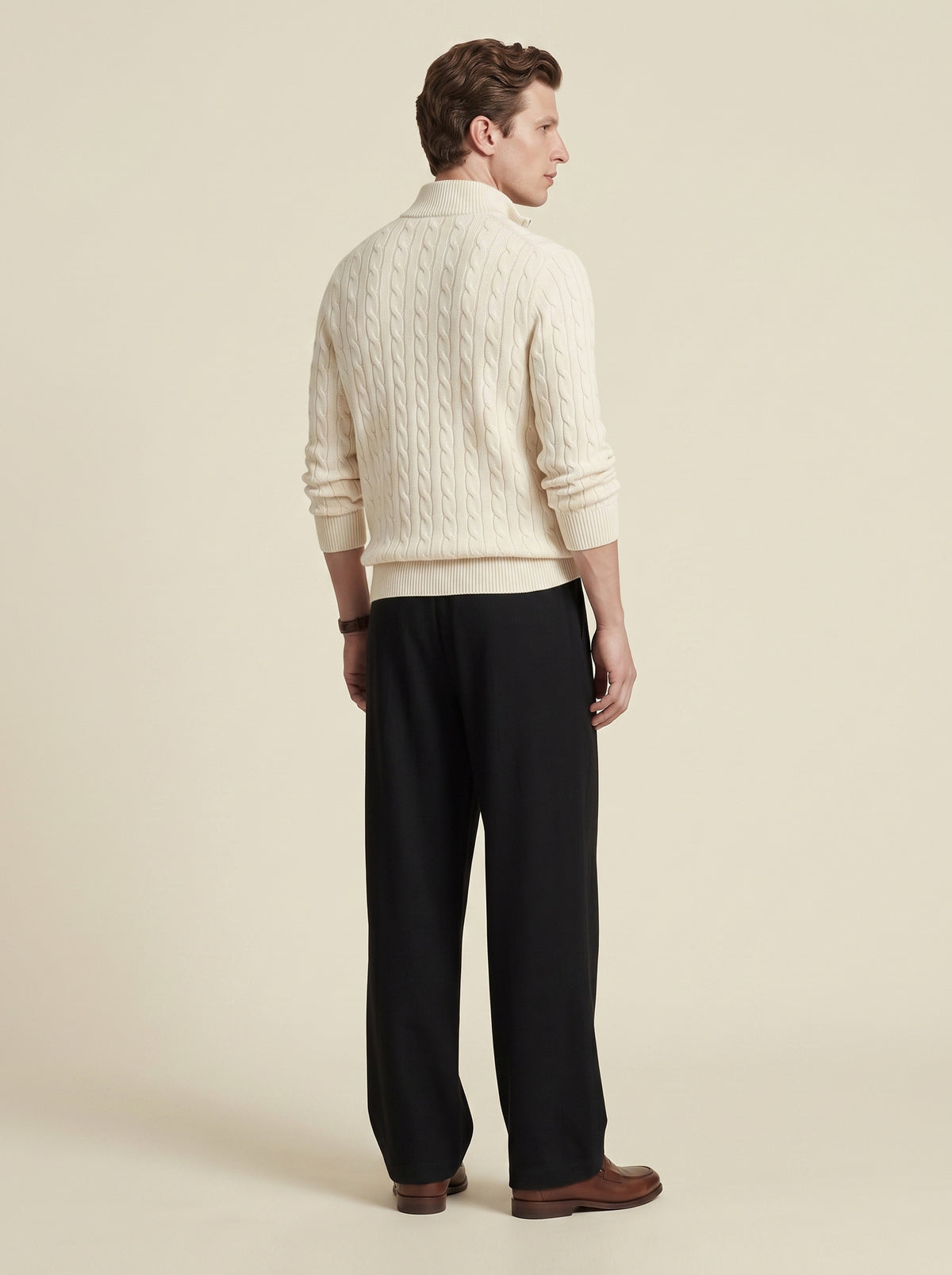 #Jet-Black_group A man shown from the back wearing a cream cable-knit mock-neck sweater, black trousers, and brown leather shoes, standing against a solid light beige studio background.