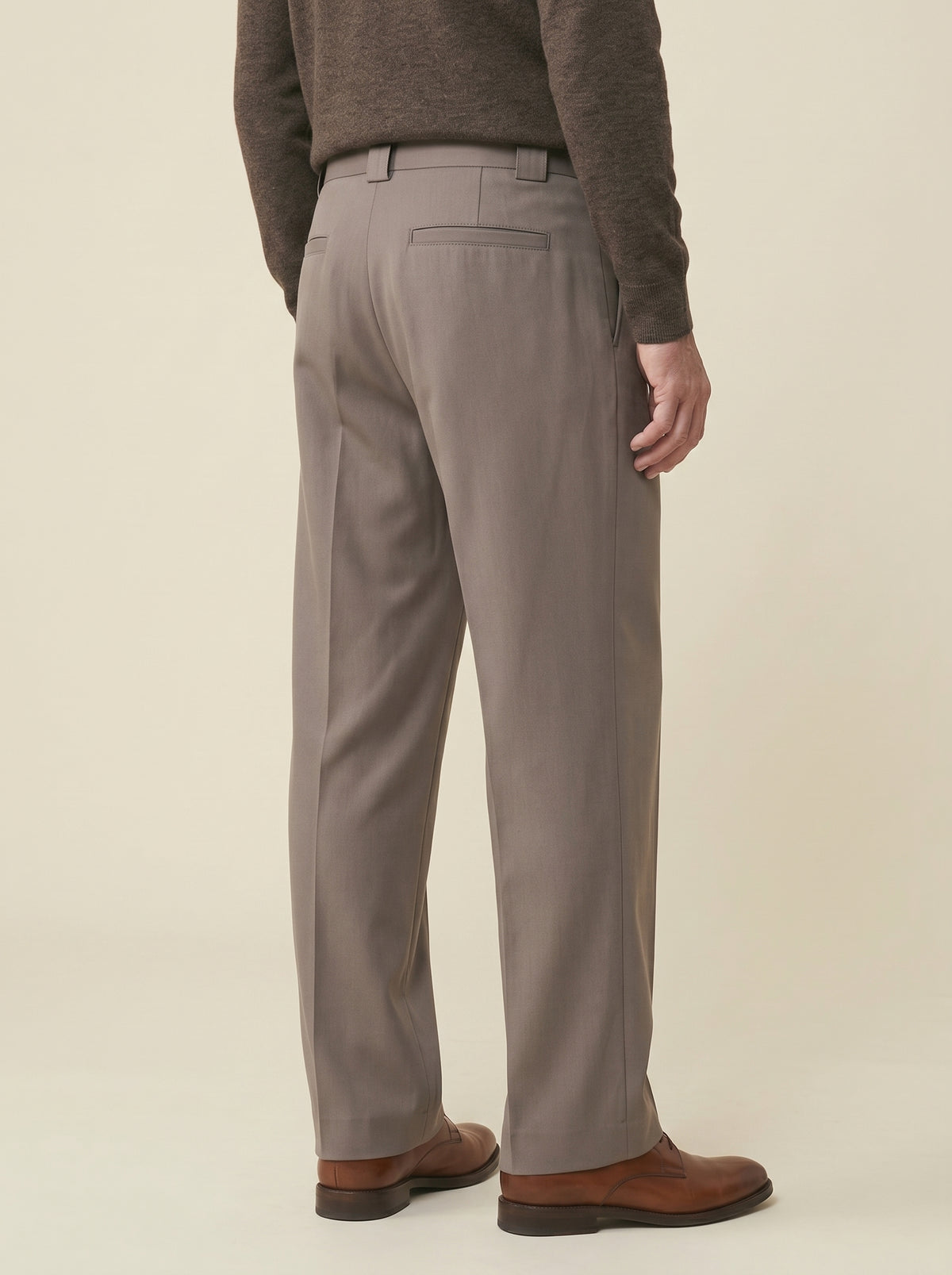 #Espresso-Brown_group A person shown from the back wearing taupe gray dress pants, a dark brown knit sweater, and brown leather shoes against a solid light beige studio background.