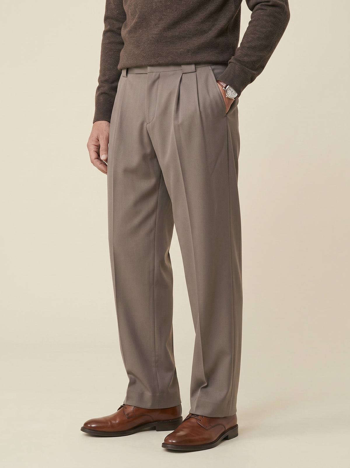 #Espresso-Brown_group A man wearing pleated gray trousers, a brown knit sweater, and brown leather dress shoes, standing against a plain beige studio background.