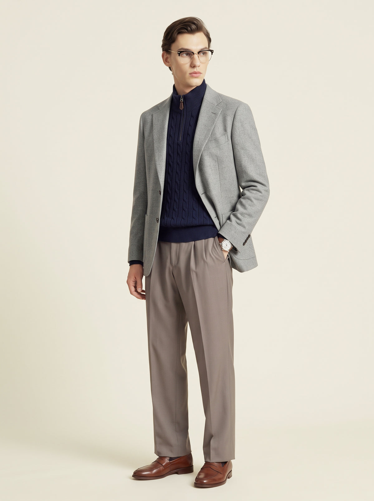 #Charcoal-Grey_group A man modeling a light gray blazer, navy blue cable-knit turtleneck, taupe trousers, and brown leather dress shoes against a solid cream background.