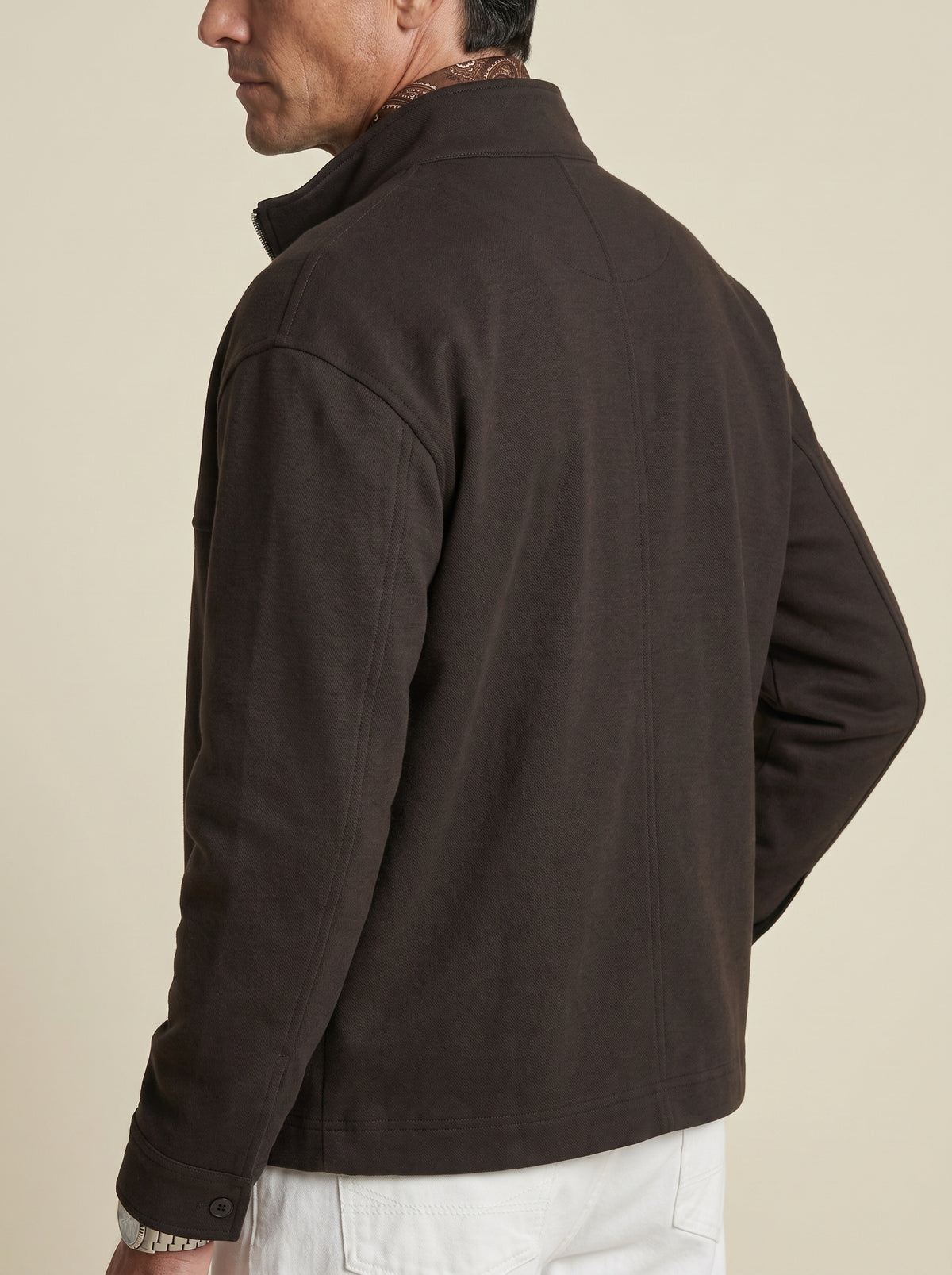 #Cedar-Brown_group A man wearing a dark brown quarter-zip jacket, shown from a side-back angle against a solid light beige background.