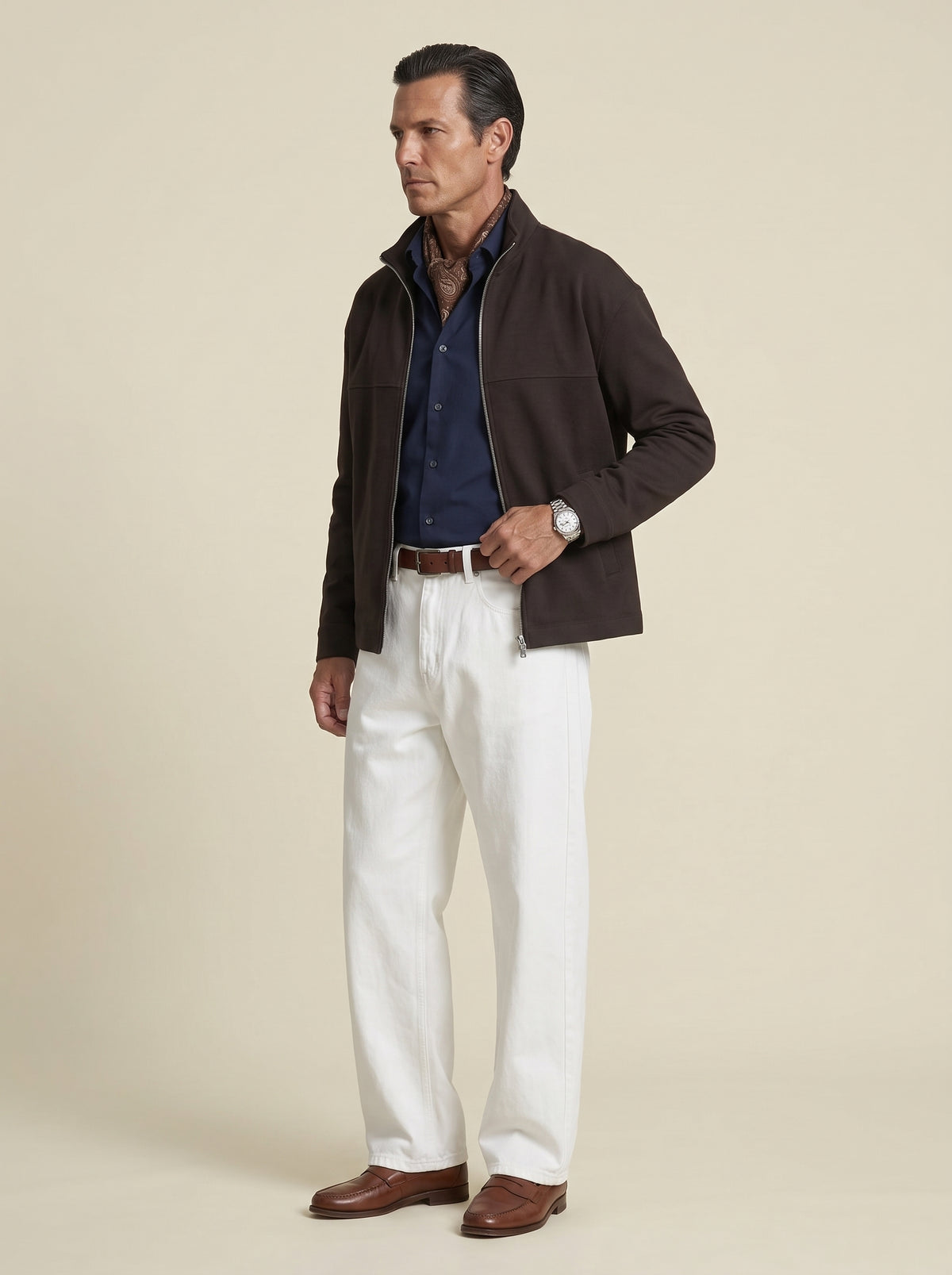 #Cedar-Brown_group A man modeling a dark brown zip-up jacket over a navy blue shirt, paired with white trousers and brown leather shoes, against a solid beige background.
