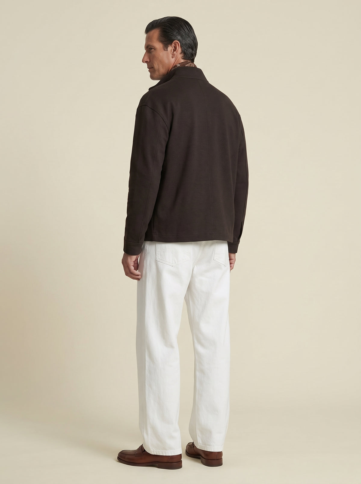 #Cedar-Brown_group A man shown from the back wearing a dark brown quarter-zip fleece jacket, white trousers, and brown leather loafers, standing against a solid light beige studio background.