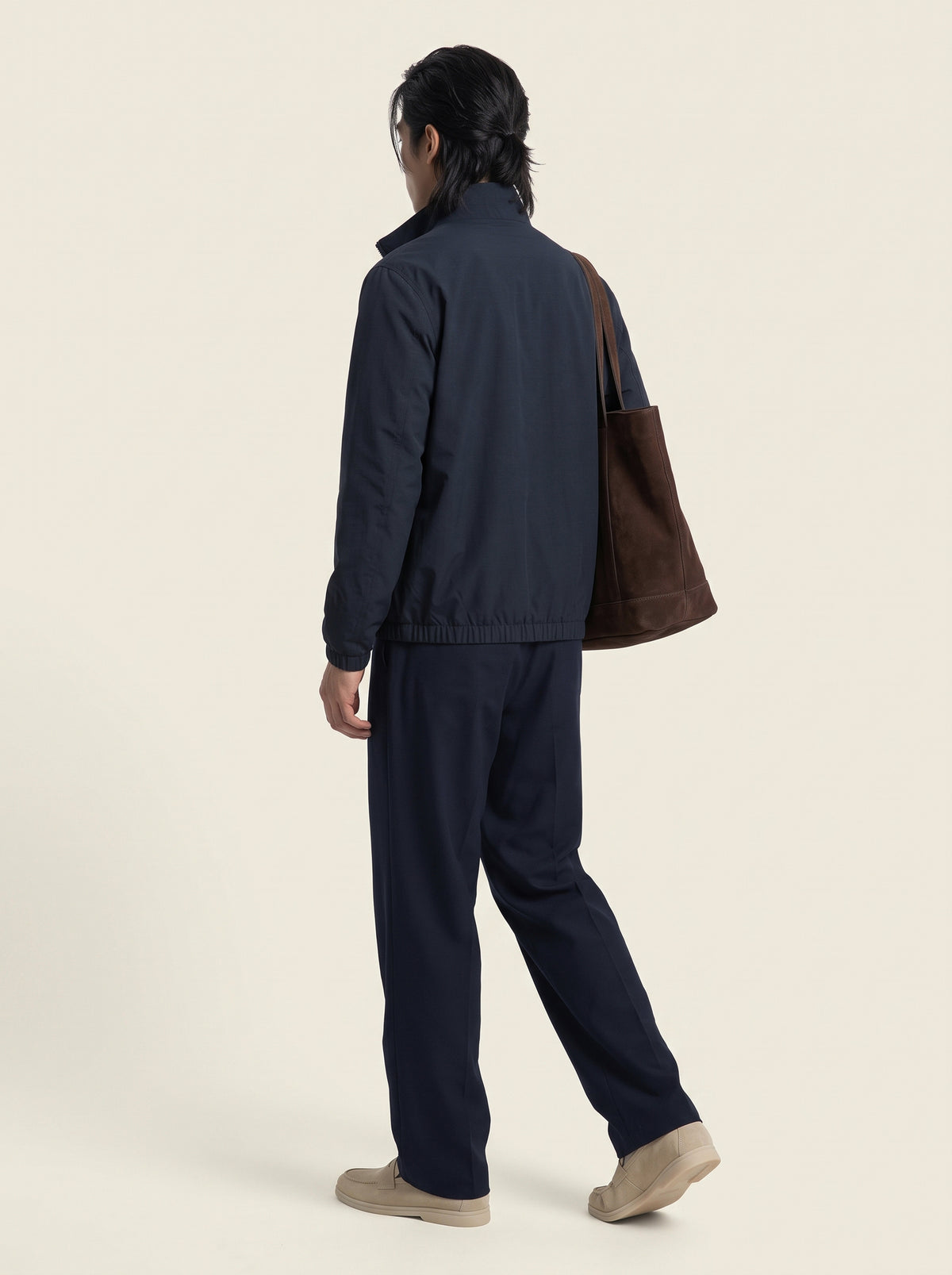 #Blue-Navy_group A model shown from the back wearing a dark navy blue jacket and matching pants, carrying a brown canvas tote bag over their shoulder, set against a plain off-white studio background.