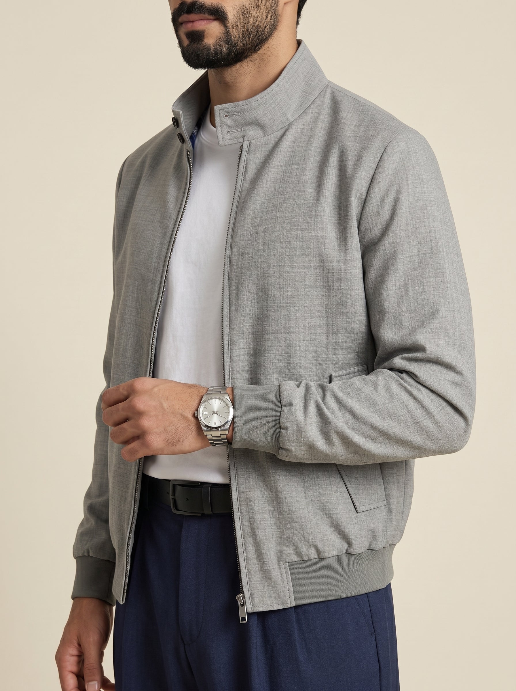 #Charcoal-Grey_group A man wearing a light gray textured zip-up jacket with a stand collar, layered over a white t-shirt and navy blue trousers, photographed against a solid beige background.