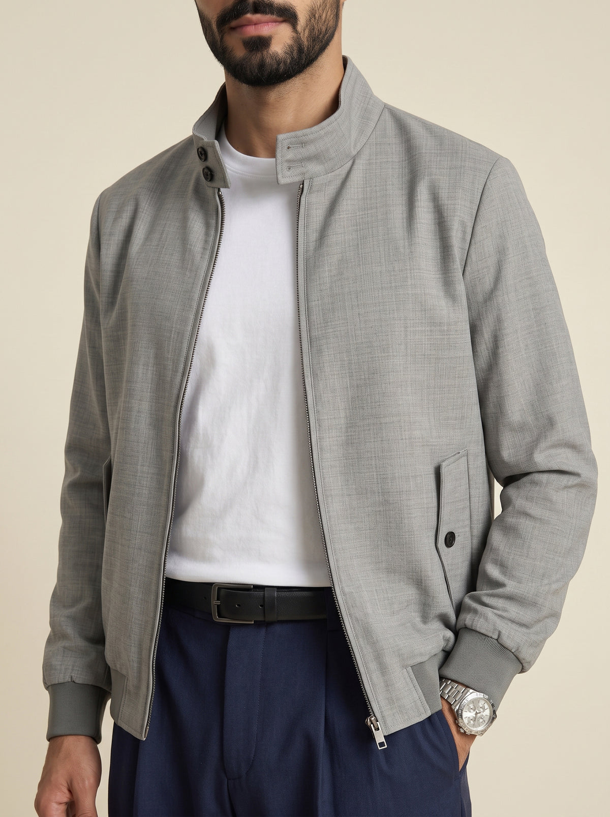 #Charcoal-Grey_group A man wearing a light gray textured zip-up jacket with a stand collar, layered over a white t-shirt and navy blue trousers, photographed against a solid beige background.