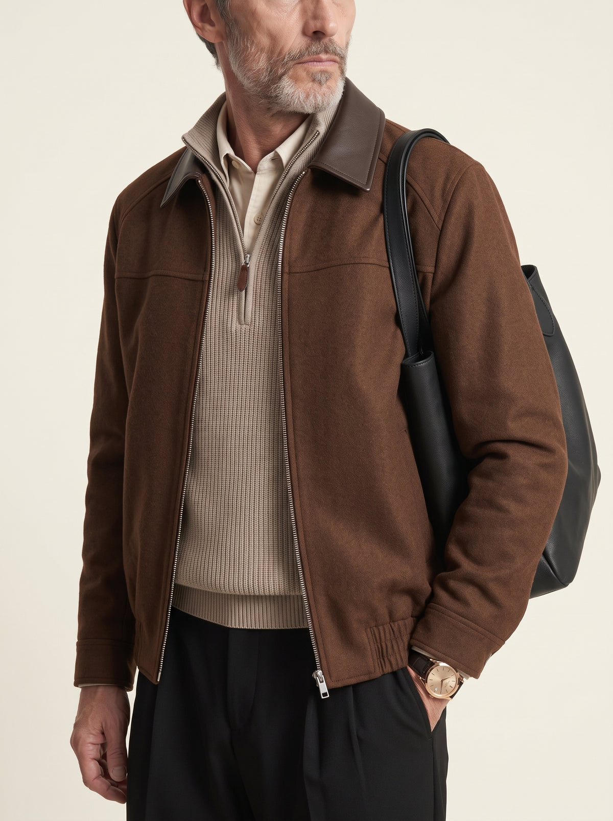#Cedar-Brown_group A man wearing a brown suede-like zip-up jacket with dark brown collar and sleeve trim, layered over a beige ribbed quarter-zip sweater and black trousers, carrying a black shoulder bag against a light beige studio background.