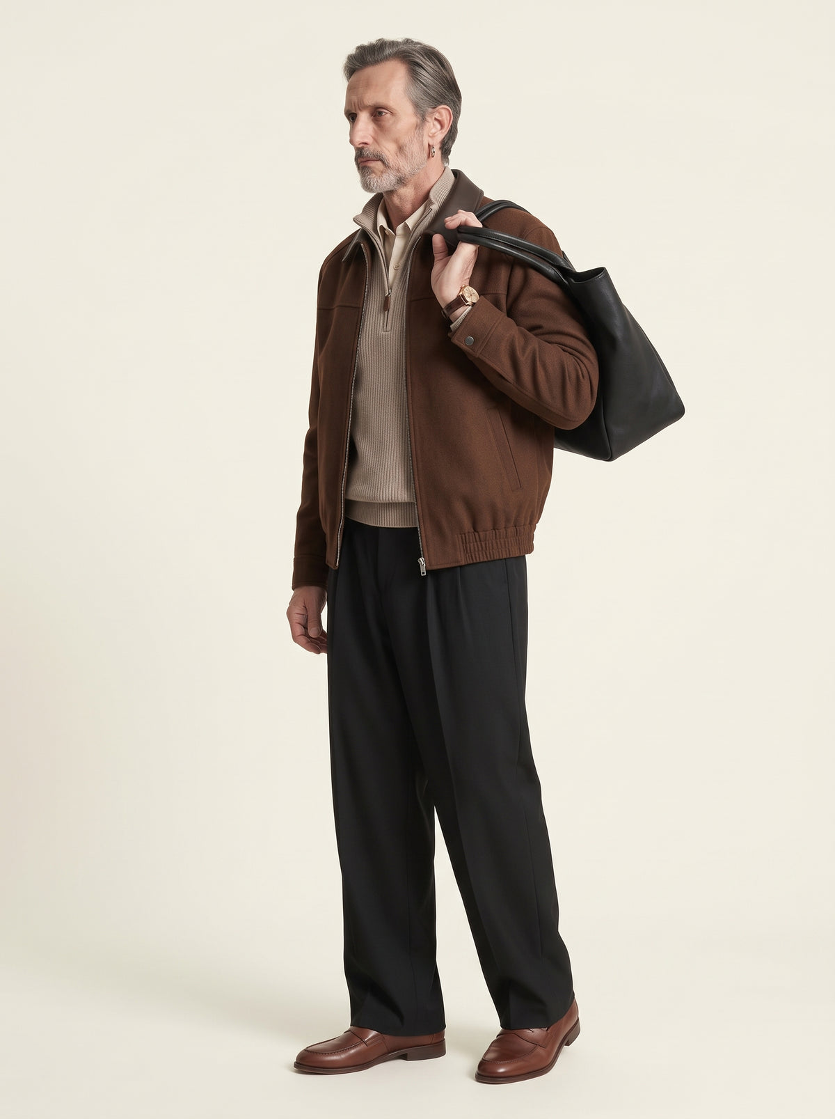 #Cedar-Brown_group A man stands in profile wearing a brown suede jacket over a beige zip-up sweater, black trousers, and brown leather loafers, while carrying a large black tote bag over his shoulder against a plain light beige studio background.