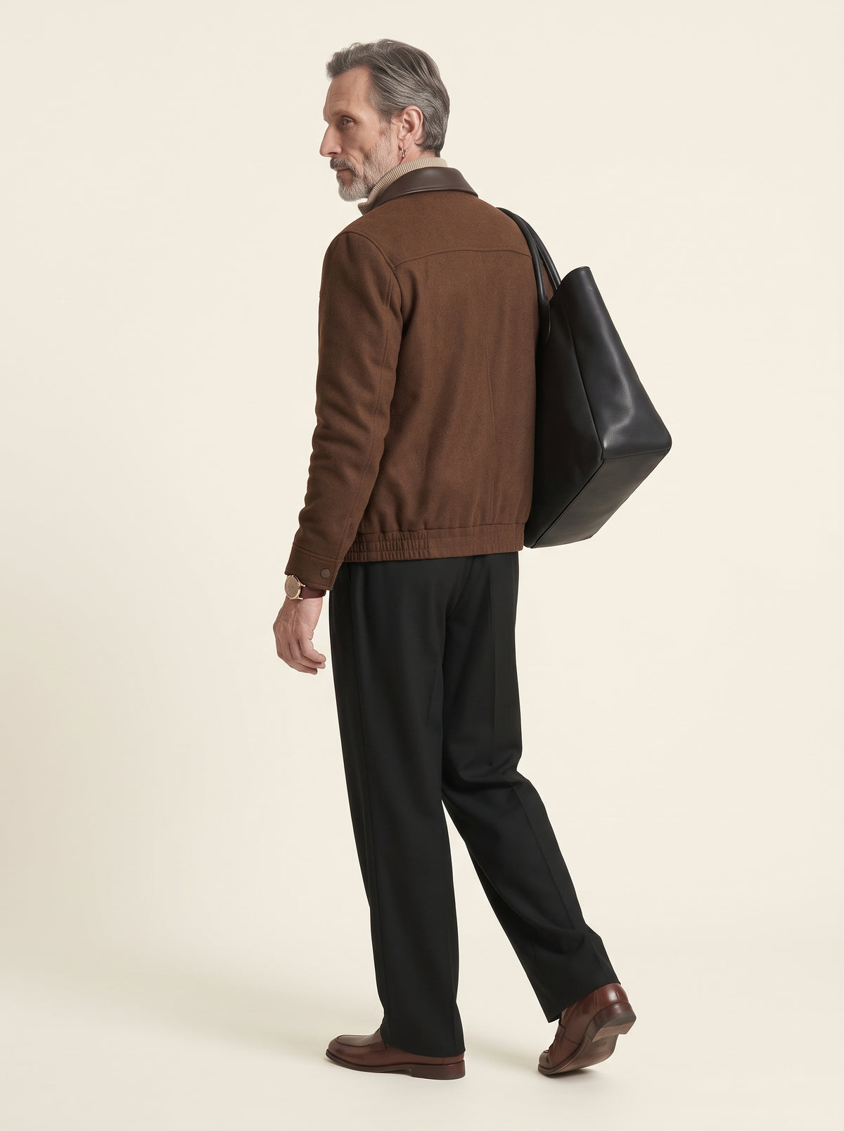 #Cedar-Brown_group A man shown from the back wearing a brown jacket, black trousers, and brown shoes, carrying a large black leather tote bag over his shoulder against a plain cream background.
