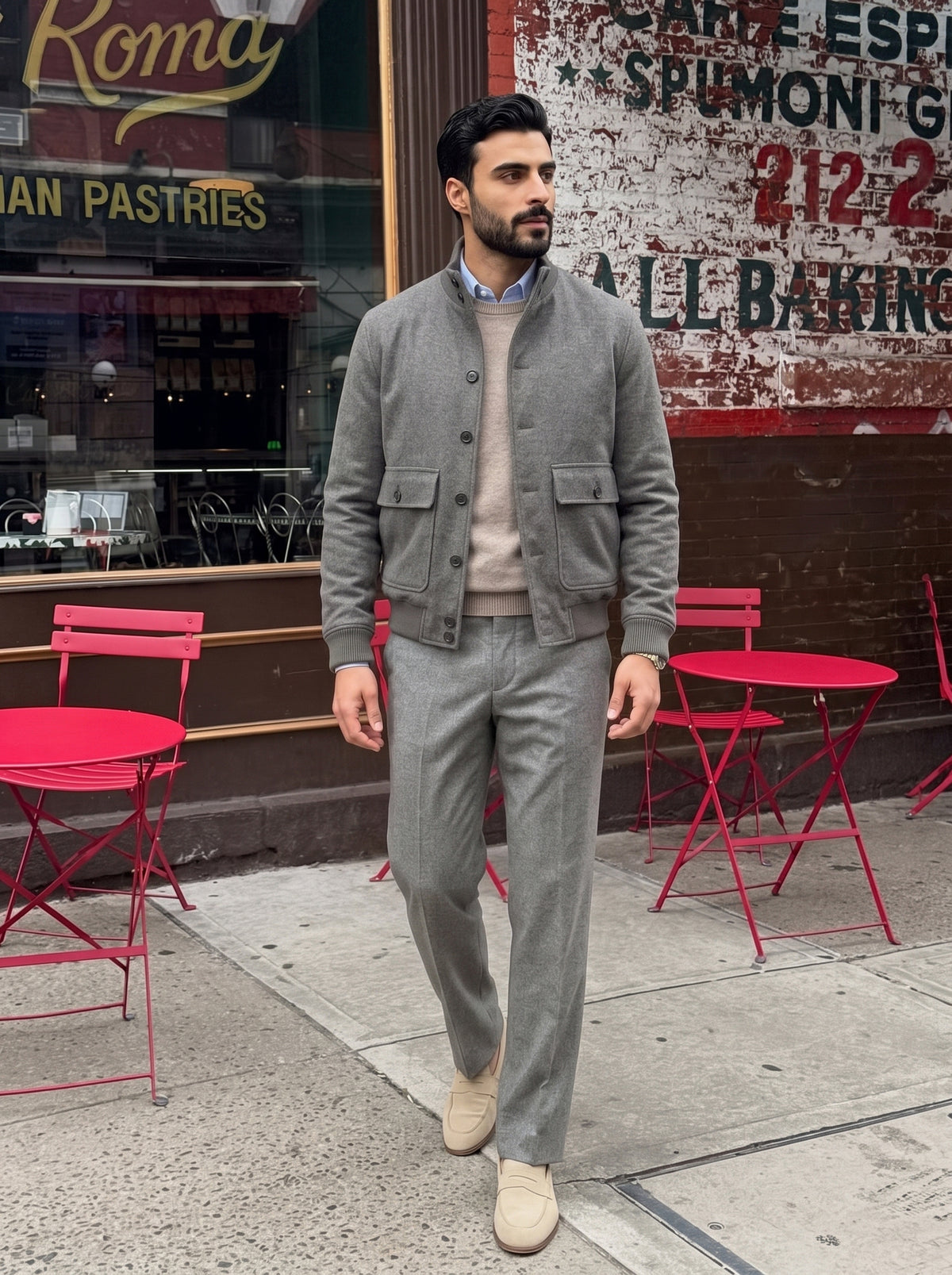 #Charcoal-Grey_group A man wearing a gray two-piece suit with a corduroy jacket and beige loafers walking on a city sidewalk in front of a bakery storefront.