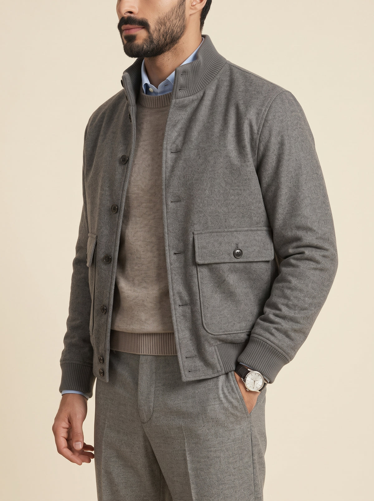 #Charcoal-Grey_group A man wearing a gray knit button-front jacket over a taupe sweater and matching gray trousers, photographed against a plain warm beige studio background.