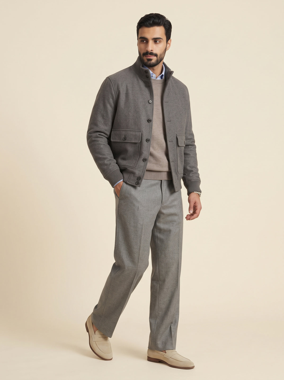 #Charcoal-Grey_group A man modeling a gray button-up cardigan over a taupe sweater, paired with matching gray trousers and beige loafers, against a solid beige studio background.