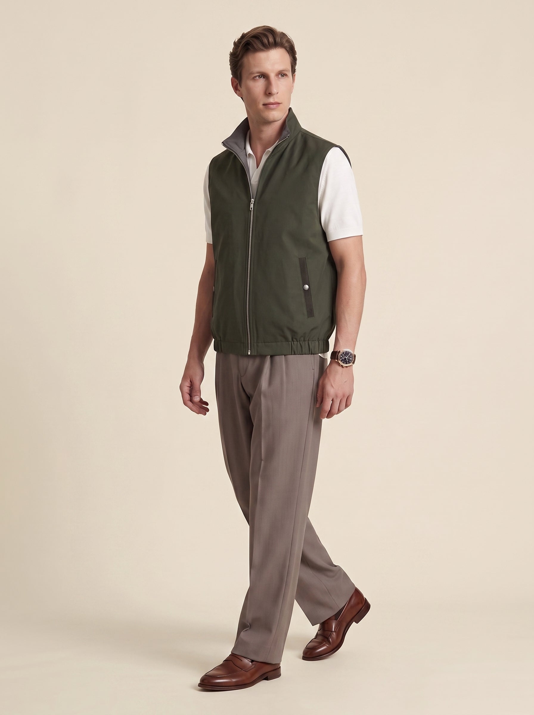 #Olive-Leaf_group A man modeling a sleeveless olive green zip-front vest over a white short-sleeve shirt, paired with taupe trousers and brown dress shoes, against a solid beige studio background.
