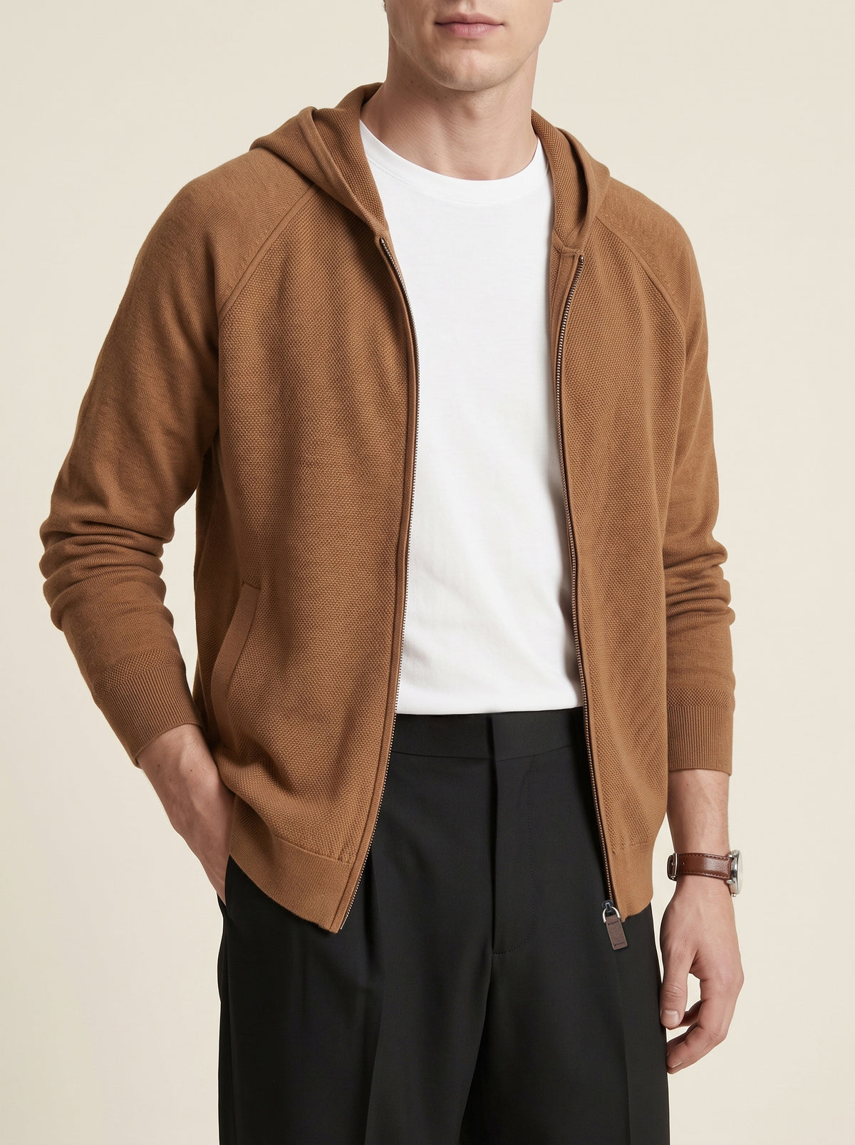 #Cedar-Brown_group A man wearing a camel brown zip-up hooded sweater over a white t-shirt and black trousers, photographed against a solid light beige background.