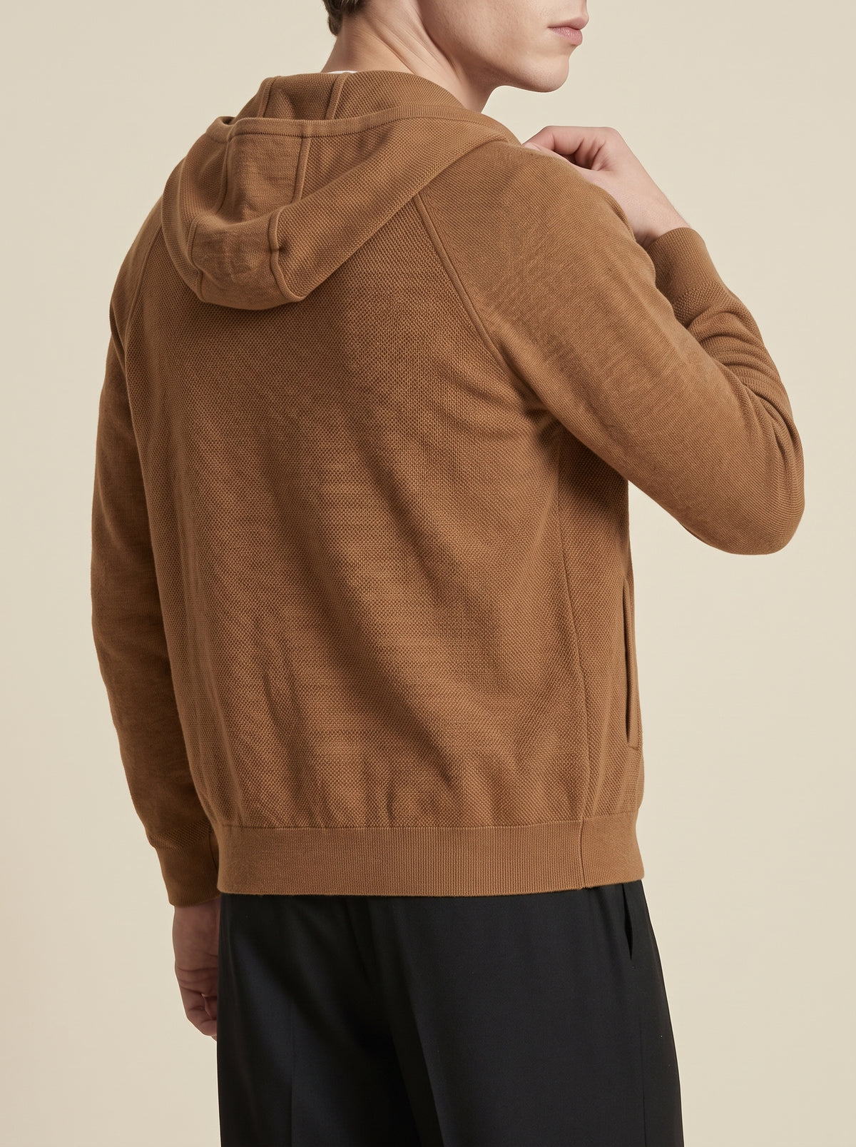 #Cedar-Brown_group A man wearing a brown hooded knit sweater, shown from a rear three-quarter angle against a solid light beige background.