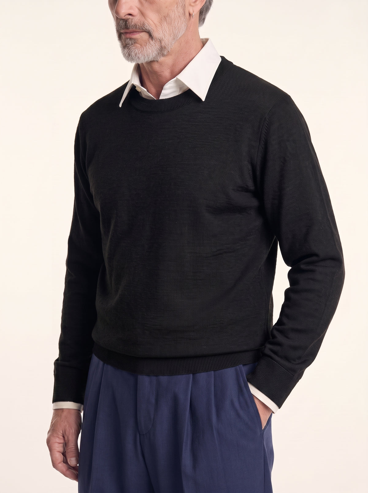 #Jet-Black_group A man wearing a black long-sleeve crewneck sweater over a white collared shirt and navy blue trousers, photographed against a plain light background.