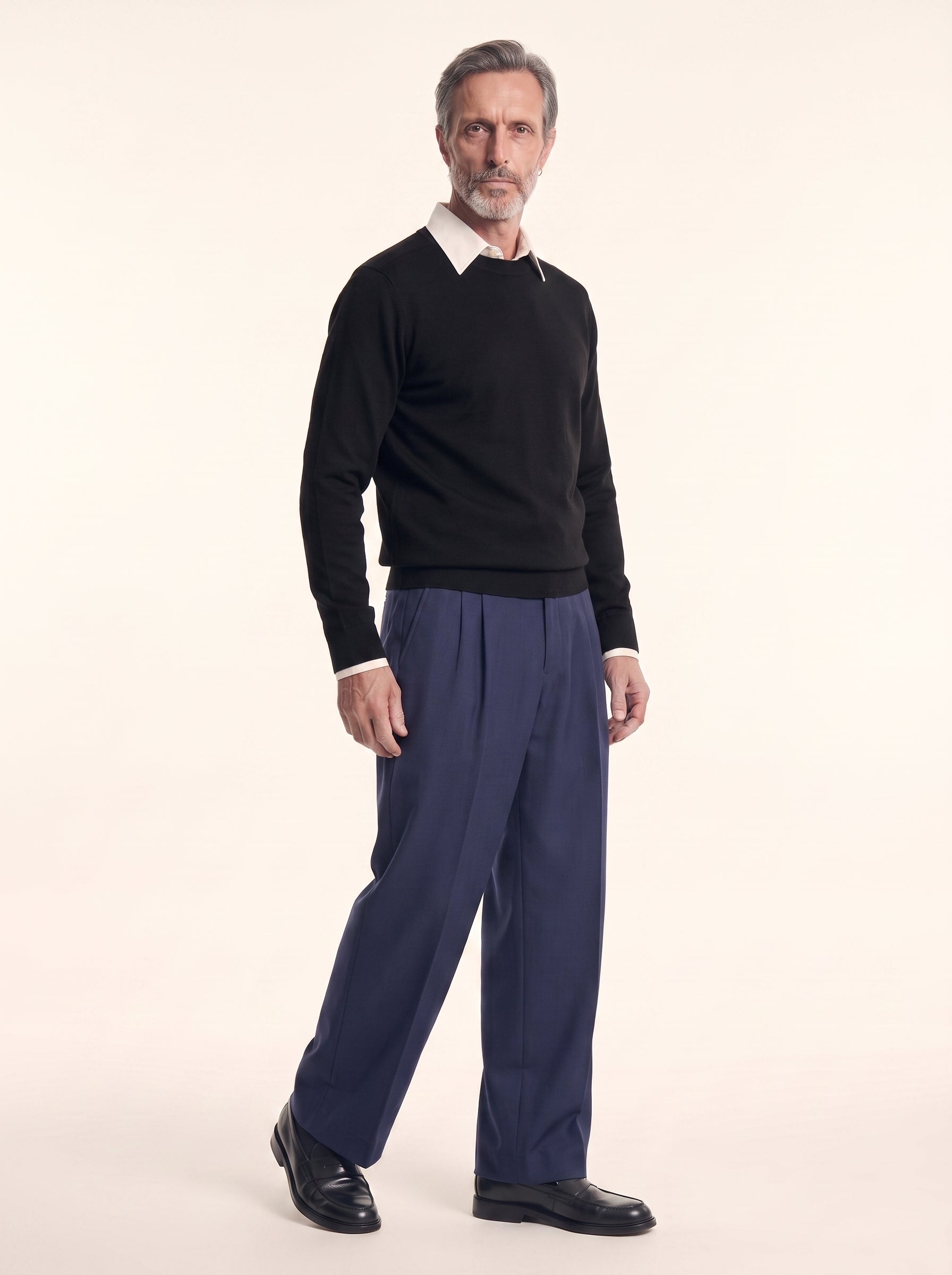 #Jet-Black_group A man modeling a black long-sleeve knit sweater over a white collared shirt, paired with navy blue trousers and black leather shoes, against a plain cream studio background.