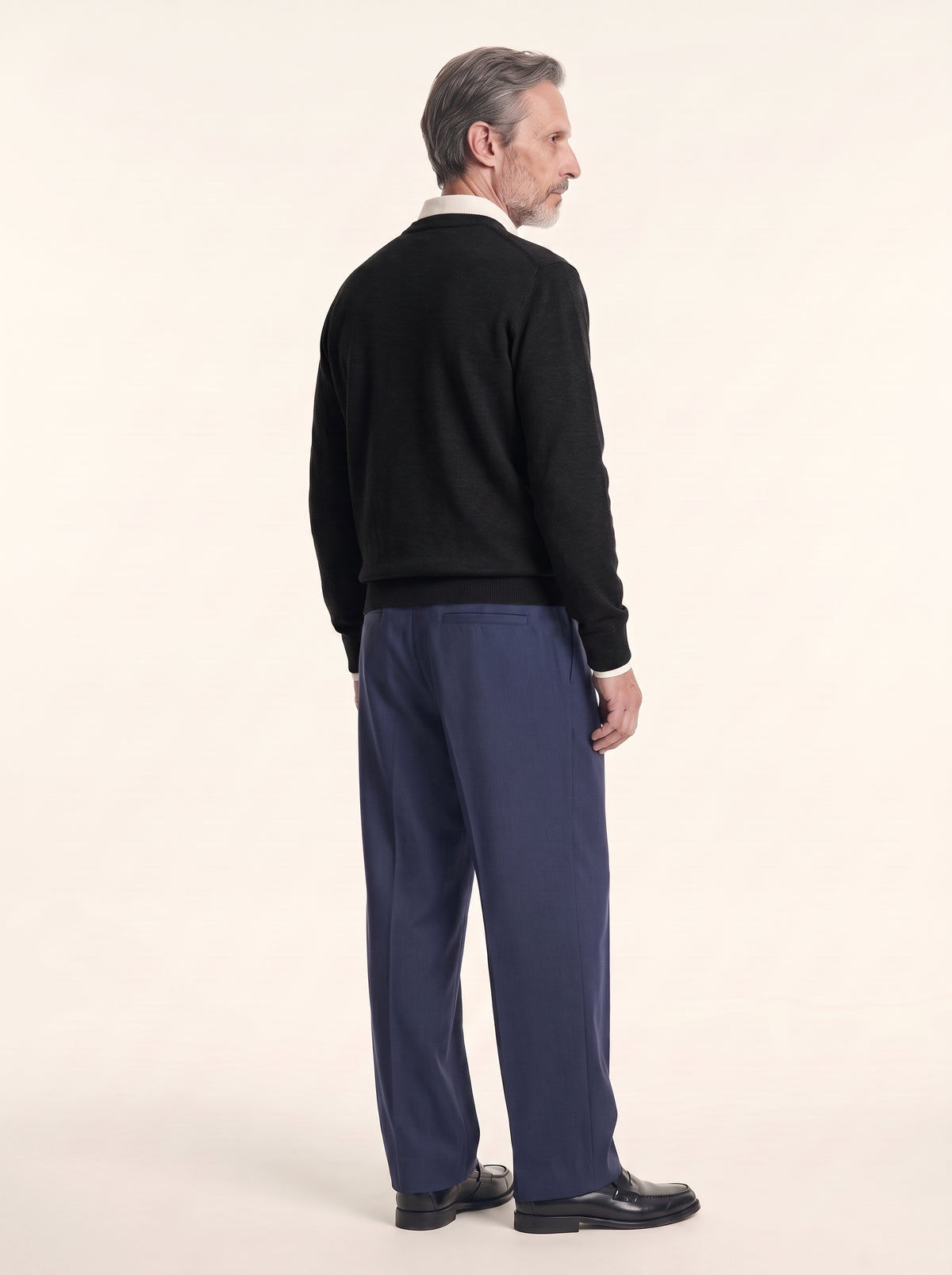 #Jet-Black_group A man shown from the back wearing a black knit sweater, navy blue trousers, and black leather shoes, standing against a plain off-white studio background.