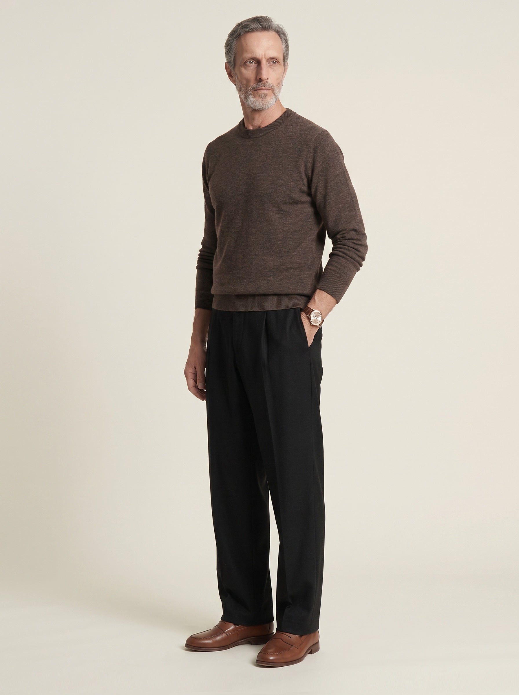 #Cedar-Brown_group A man wearing a brown crewneck knit sweater, black trousers, and brown leather shoes, standing against a plain light beige studio background.
