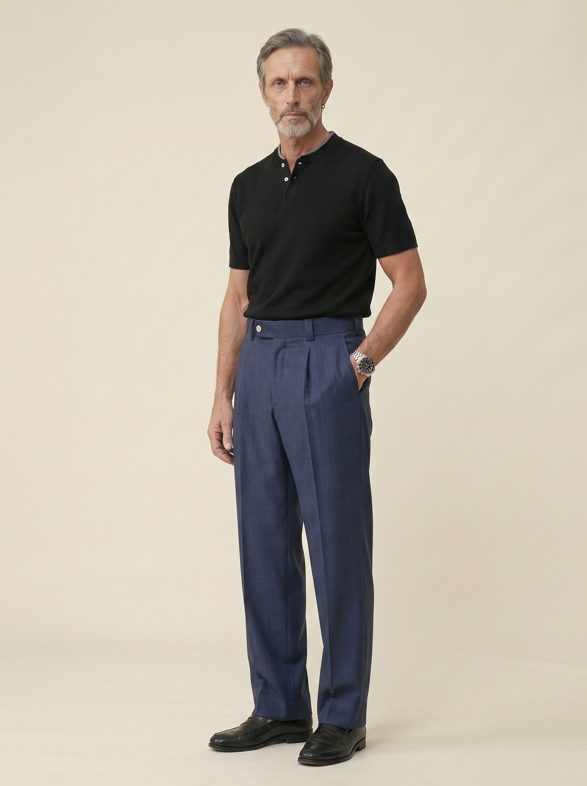 #Jet-Black_group A man modeling a black short-sleeve polo shirt and navy blue pleated trousers, standing against a solid beige studio background.