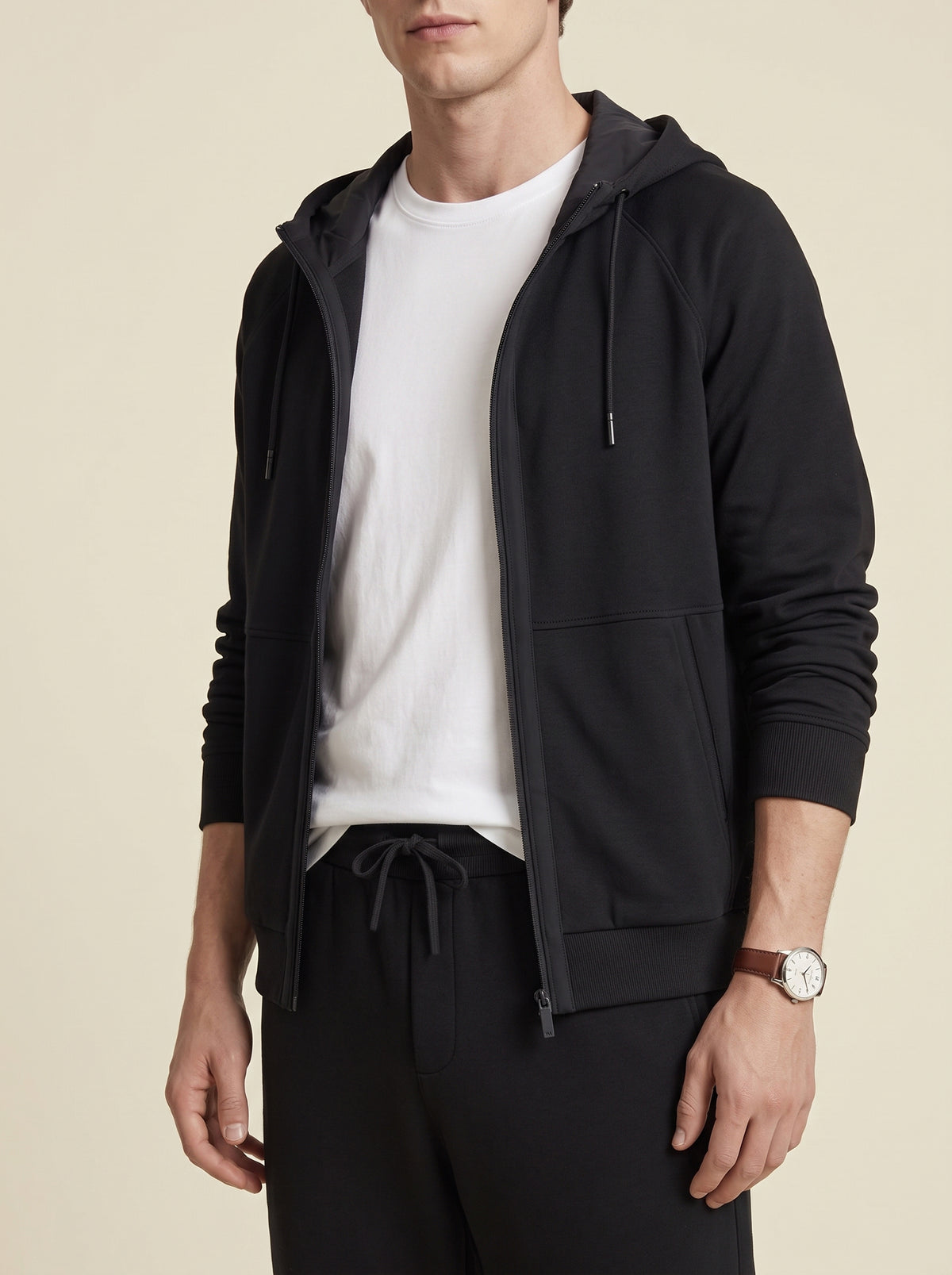 #Jet-Black_group A man wearing a black zip-up hoodie over a white t-shirt and black pants, shown from the chin down against a plain beige background.