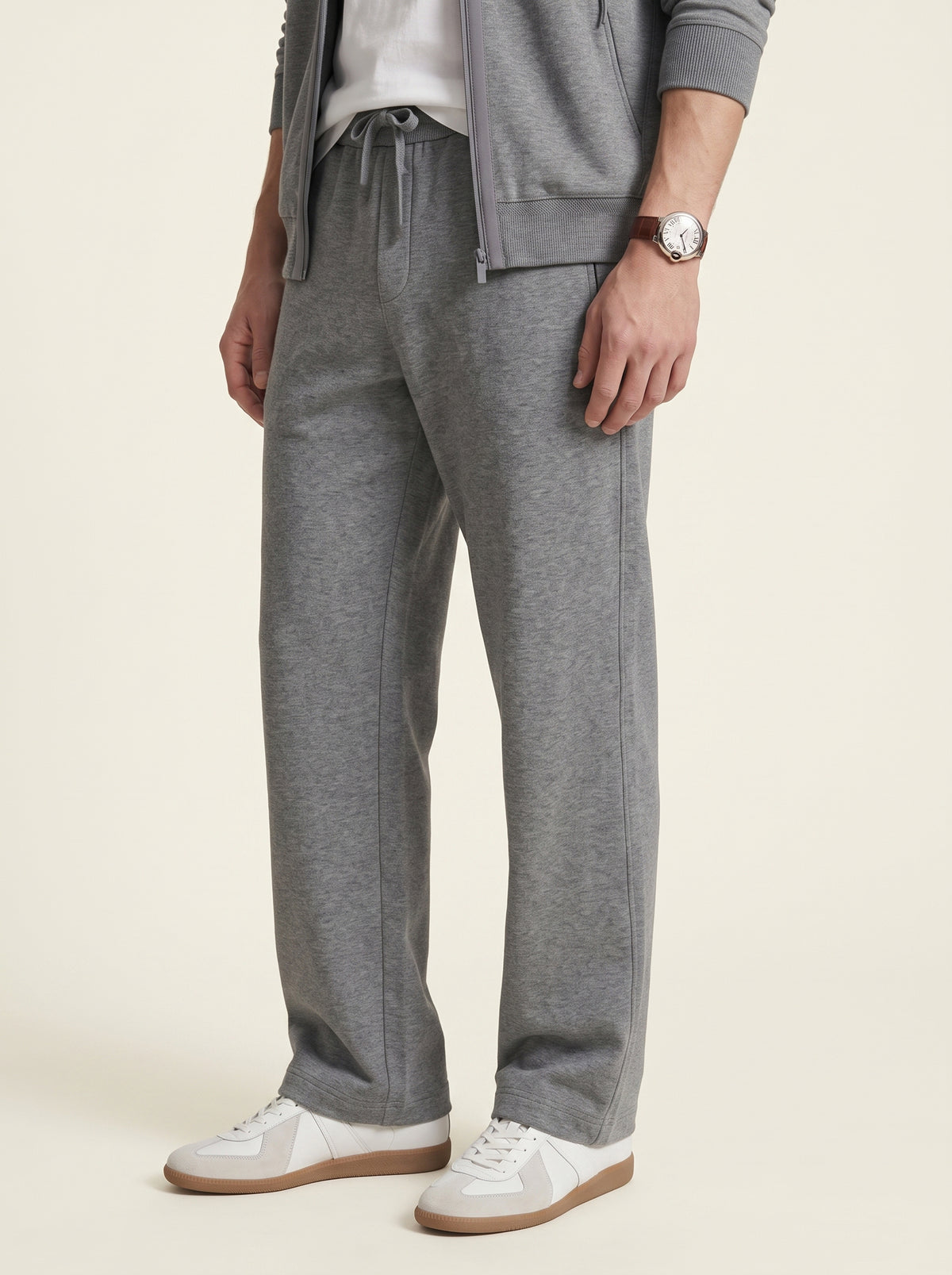 Charcoal-Grey_group A person wearing heather gray drawstring sweatpants with a matching zip-up hoodie and white sneakers, shown from the waist down against a plain light beige studio background.