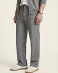 Charcoal-Grey_group A person wearing heather gray drawstring sweatpants with a matching zip-up hoodie and white sneakers, shown from the waist down against a plain light beige studio background.