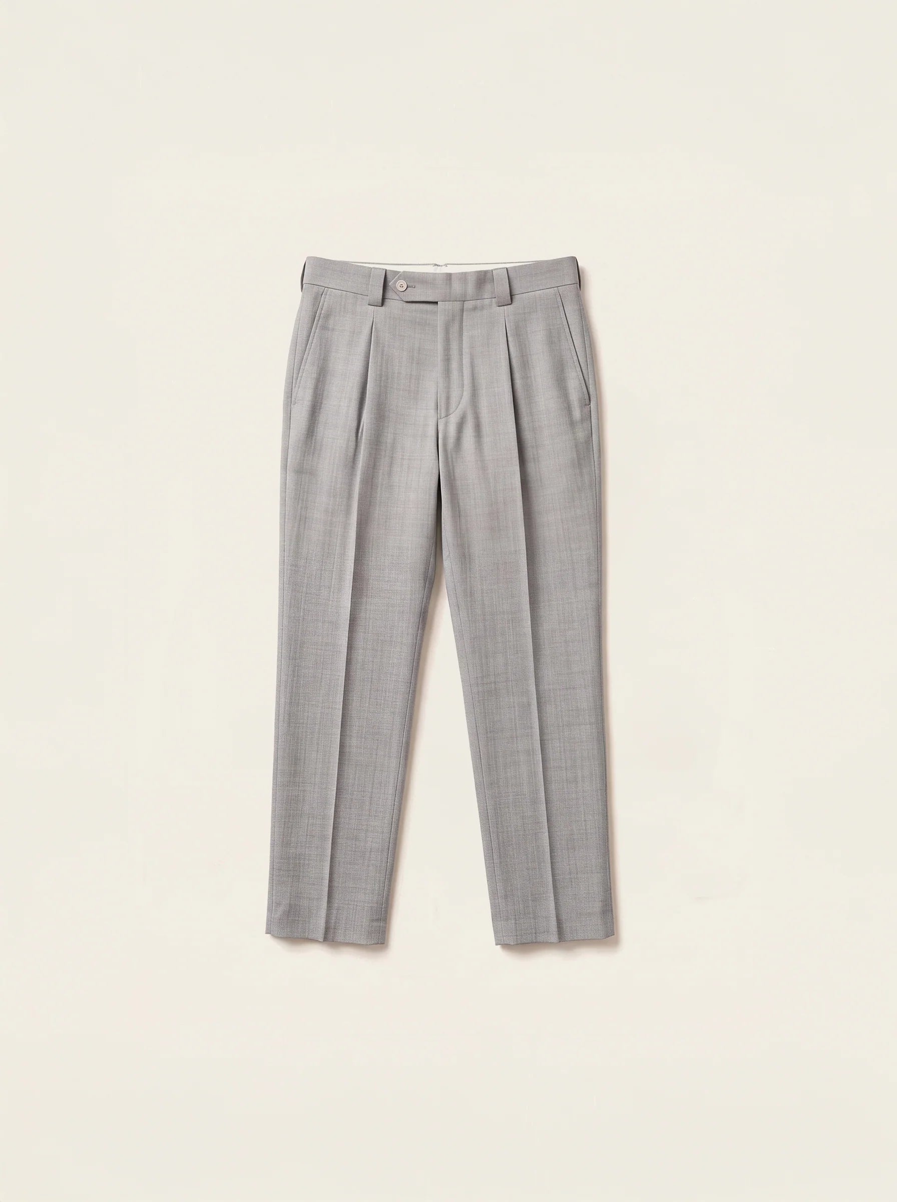 #Silver-Grey_group A pair of light gray pleated trousers laid flat against a warm off-white background.
