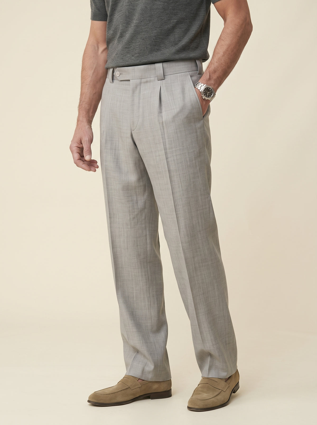 #Silver-Grey_group A man wearing light gray pleated dress pants, a dark gray t-shirt, and tan suede loafers, standing against a solid beige background.