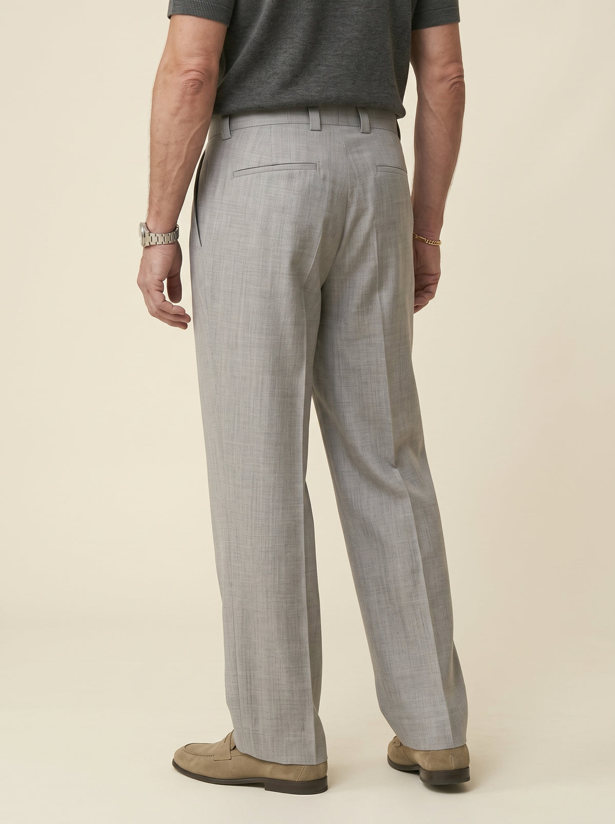 #Silver-Grey_group A man shown from the back wearing light gray tailored trousers, a dark gray short-sleeve shirt, and tan loafers against a plain warm beige studio background.