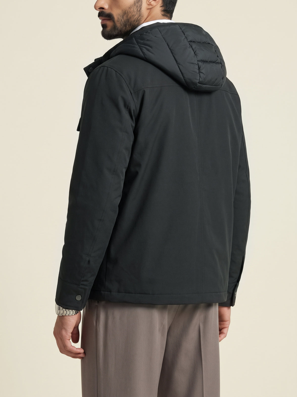 #Slate-Grey_group A man wearing a black hooded jacket, shown from a rear three-quarter angle against a plain beige studio background.